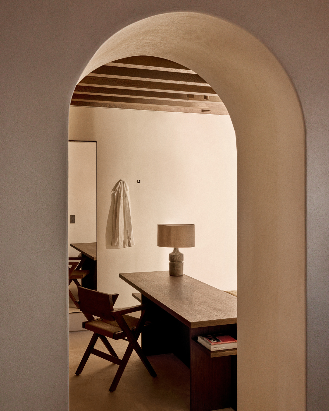 An arched doorway into a suite, plaster walls, timber beams and a writing desk.