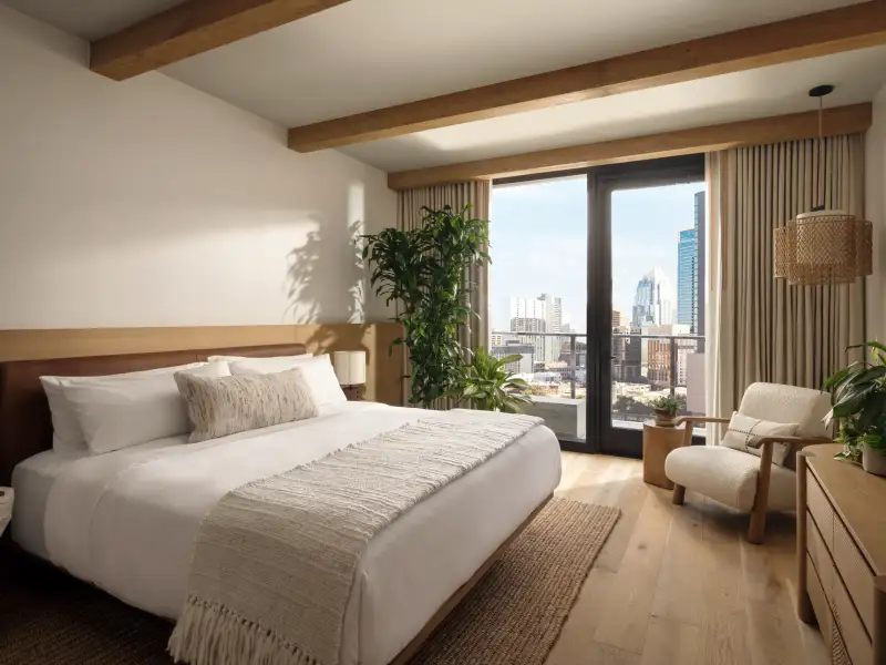 A guestroom at 1 Hotel Austin, timber beams, linen bedding and a balcony over downtown.
