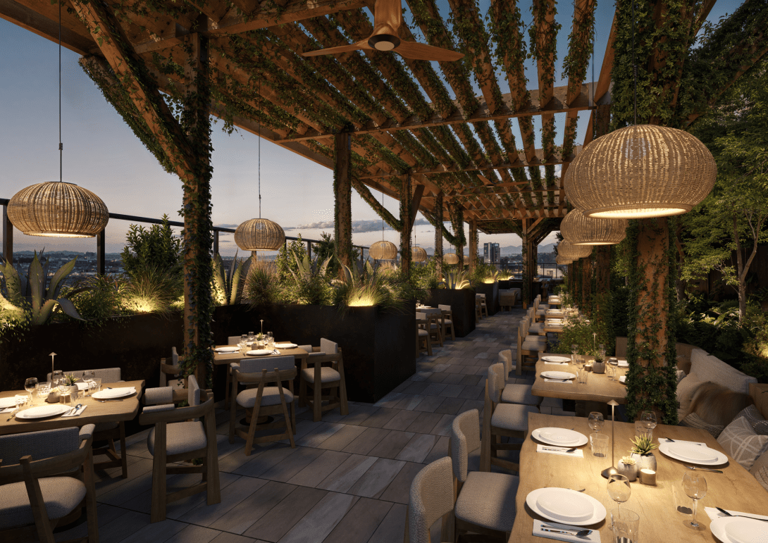 The rooftop pool bar at dusk, planted pergola and lantern light over the tables.
