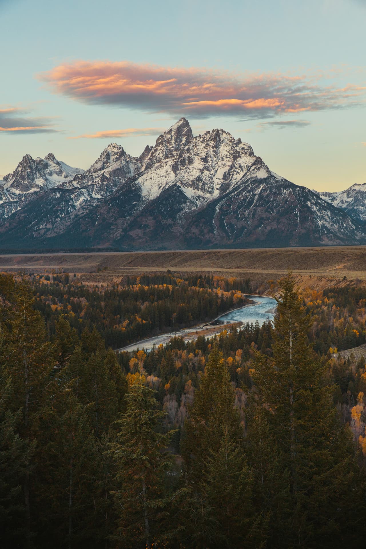 Snow-capped peaks above an autumn valley and a winding river at dusk