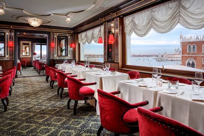 The dining room at the Danieli, red velvet chairs and windows onto the lagoon and the Doge's Palace.