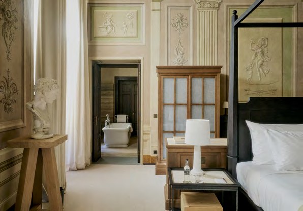 A bedroom with restored frescoed walls and a freestanding bath at La Réserve Firenze.