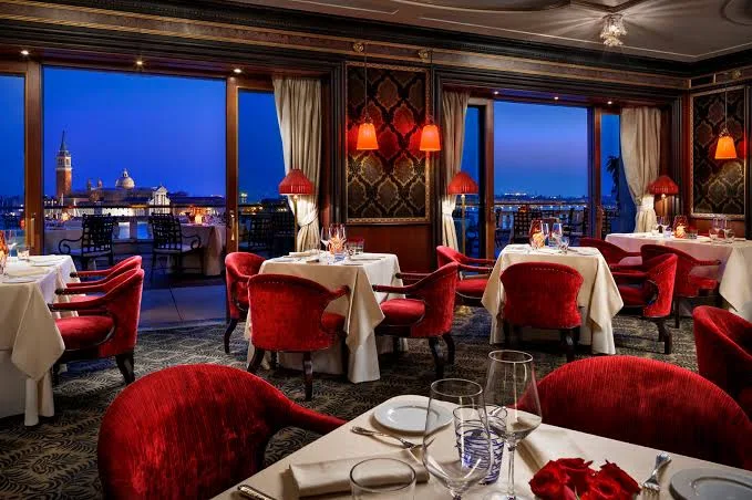 The Danieli dining room after dark, lamplight and the lagoon lit beyond the windows.