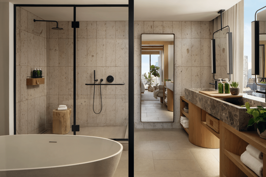 A guestroom bathroom in stone and oak, with a freestanding tub and a walk-in shower.