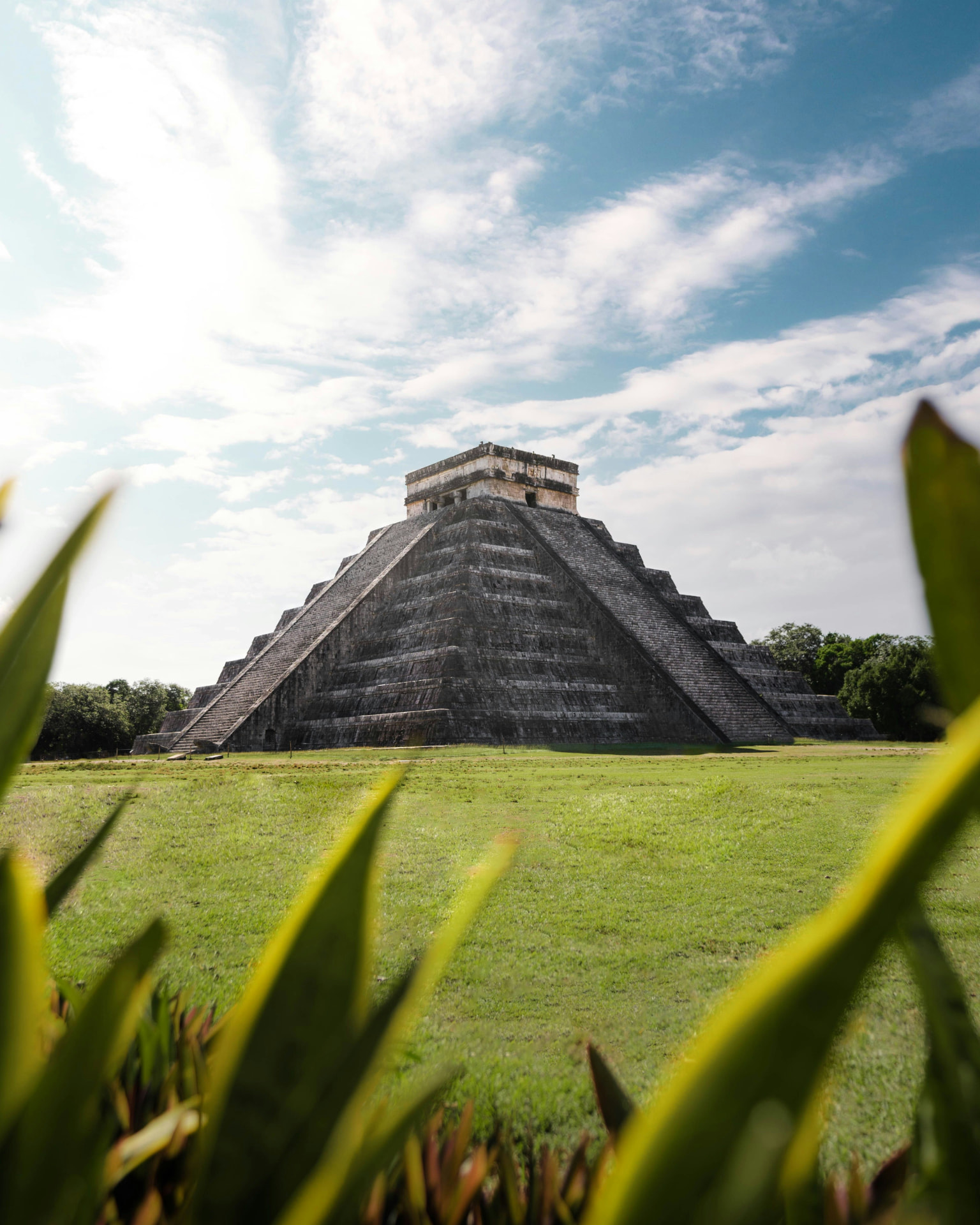 The Maya pyramid of Chichen Itza rising above green grass and tropical foliage